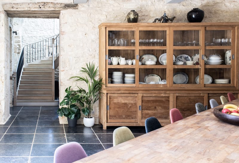 Stone-walled dining room with oak display cabinet, communal table, and mismatched upholstered chairs
