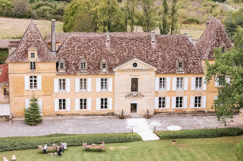 Aerial view of French chateau with ochre limestone walls, white shutters, and terracotta mansard roof