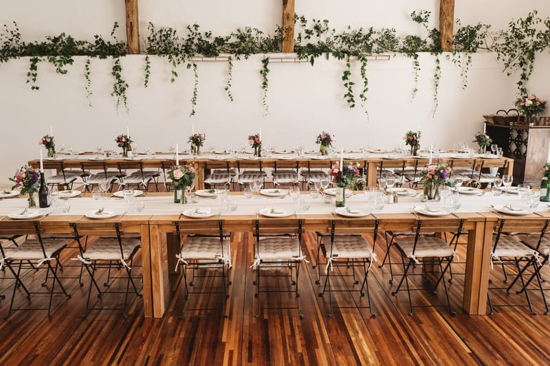 Barn reception farm tables with black chairs blush and mauve bud vase centerpieces cascading ivy garland on white walls