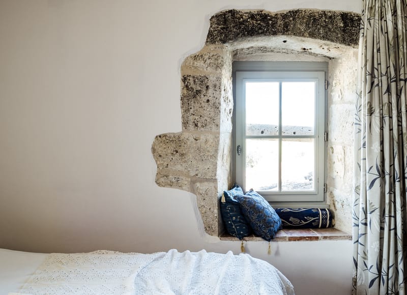 Deep-set limestone window with navy embroidered cushions botanical curtain and broderie anglaise bed