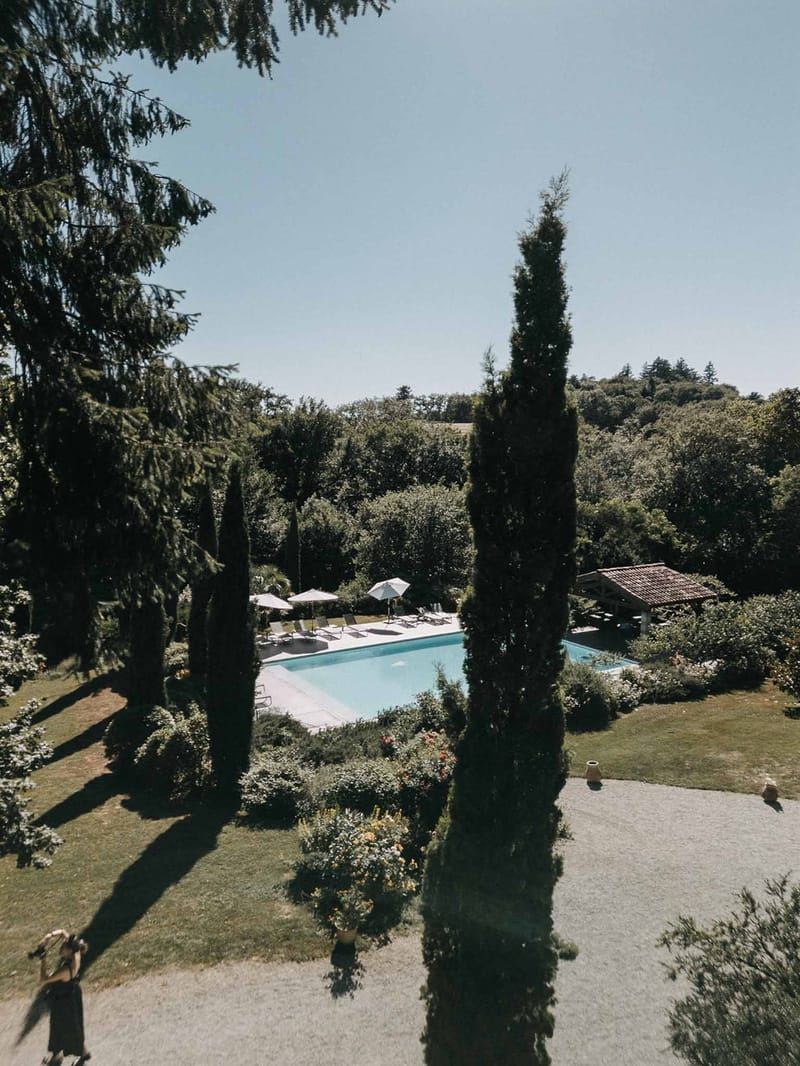 Elevated view of venue grounds with rectangular pool, sun loungers, cypress trees, and covered pergola