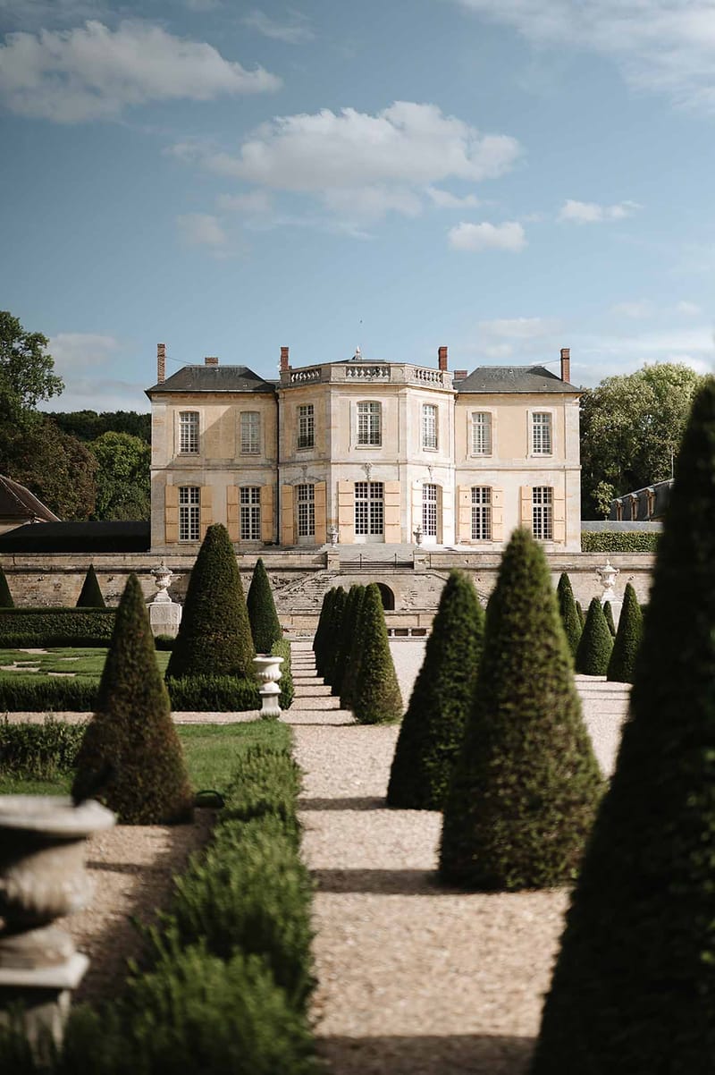 French chateau with golden limestone facade and formal parterre garden with topiary yews and gravel pathways