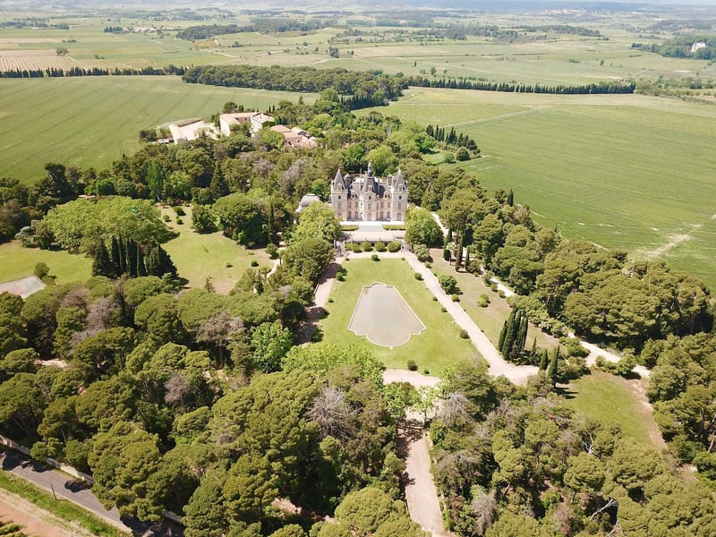 Aerial view of white turreted chateau with formal garden axis, reflecting pool, and surrounding vineyards
