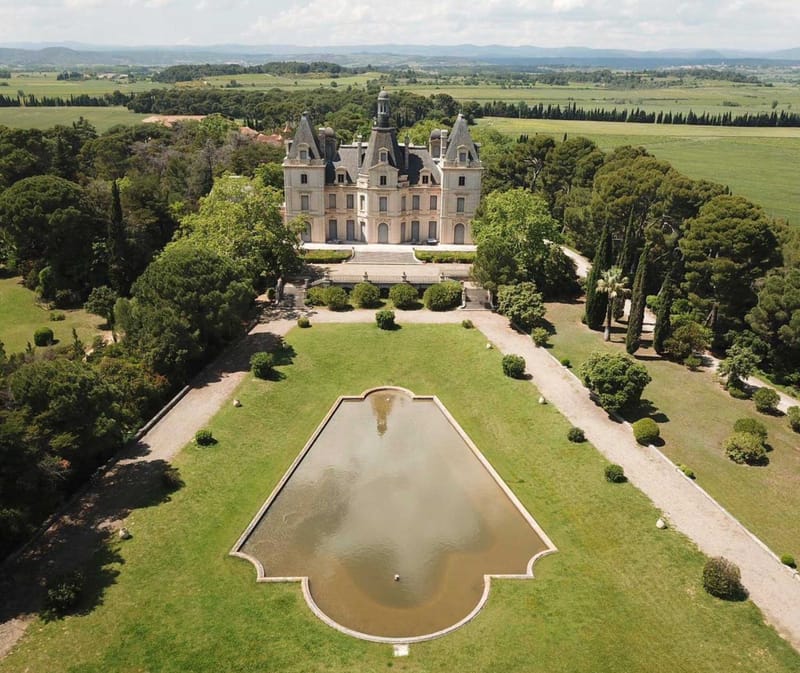 Aerial Second Empire chateau with slate towers, ornamental pond, formal topiary, and rolling countryside beyond