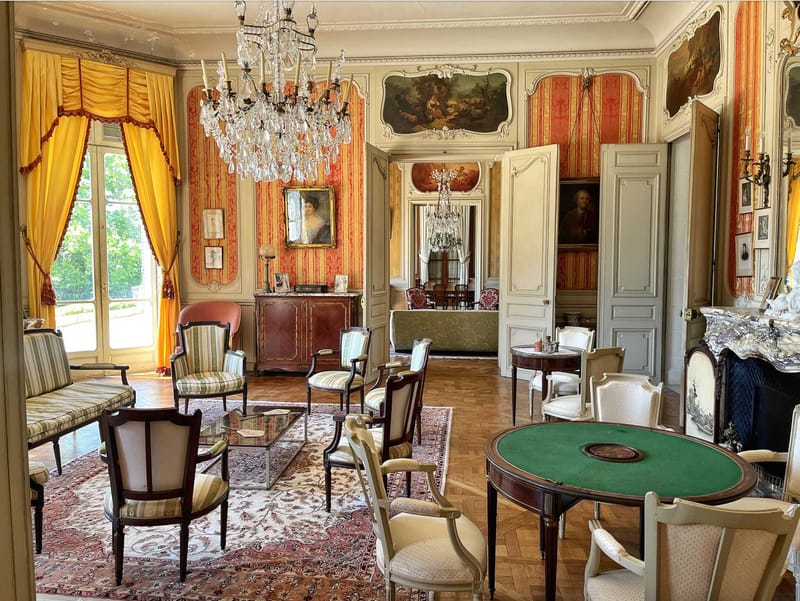 Grand salon inside a French chateau with crystal chandeliers, damask walls, and Louis XVI furniture