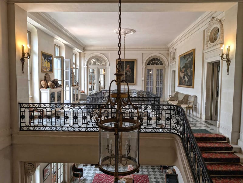 Chateau upper gallery with black and white marble floor, grand staircase, brass lantern, and gilt-framed paintings