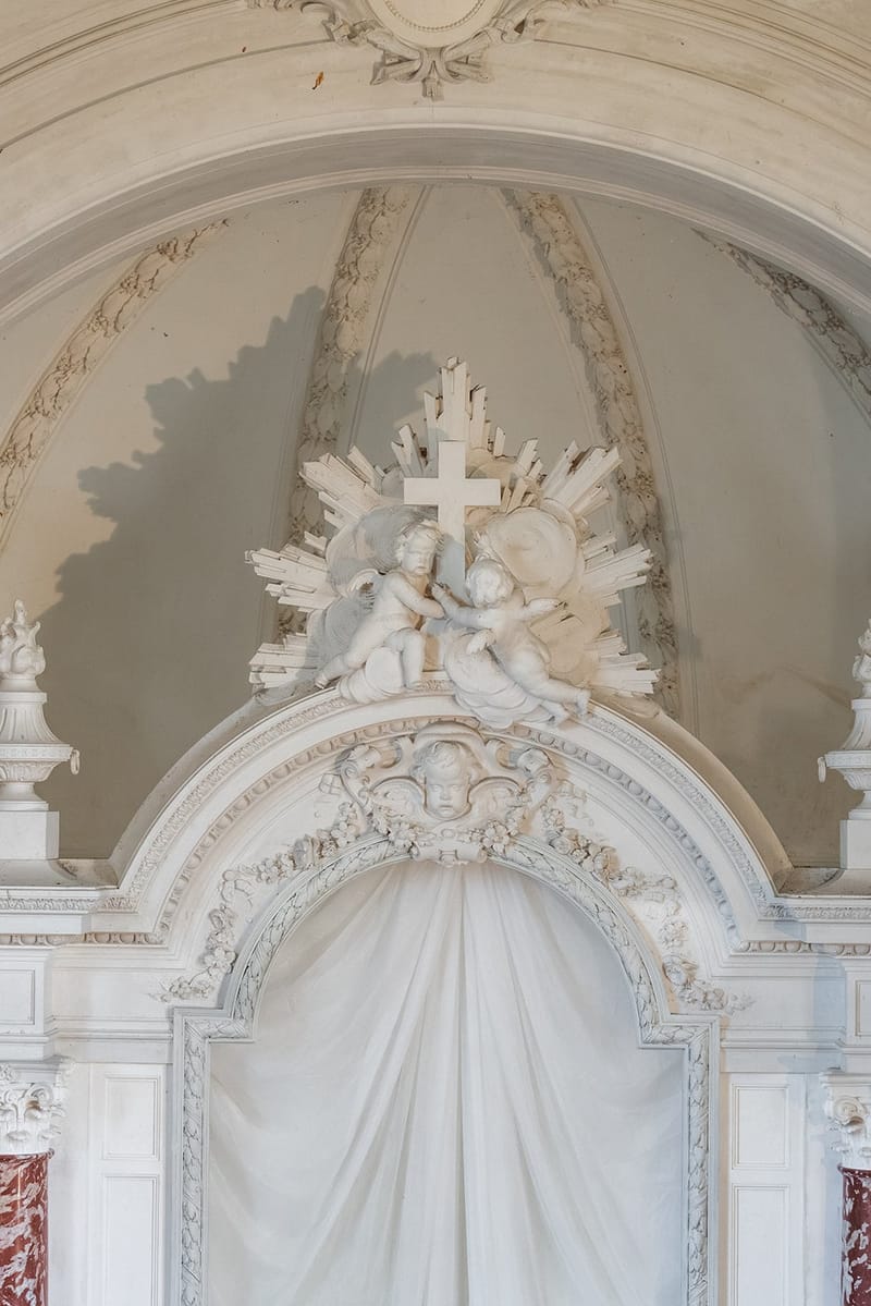 Carved cherub and cross relief above the white altar niche in Château du Terral's chapel