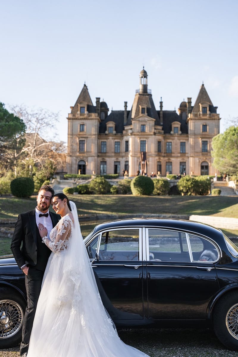 Bride and groom beside a vintage car before the turreted facade of Château du Terral