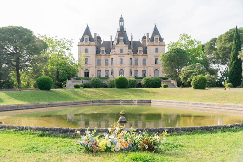 Château du Terral with turreted facade reflected in the grounds' ornamental pond and a low floral arrangement