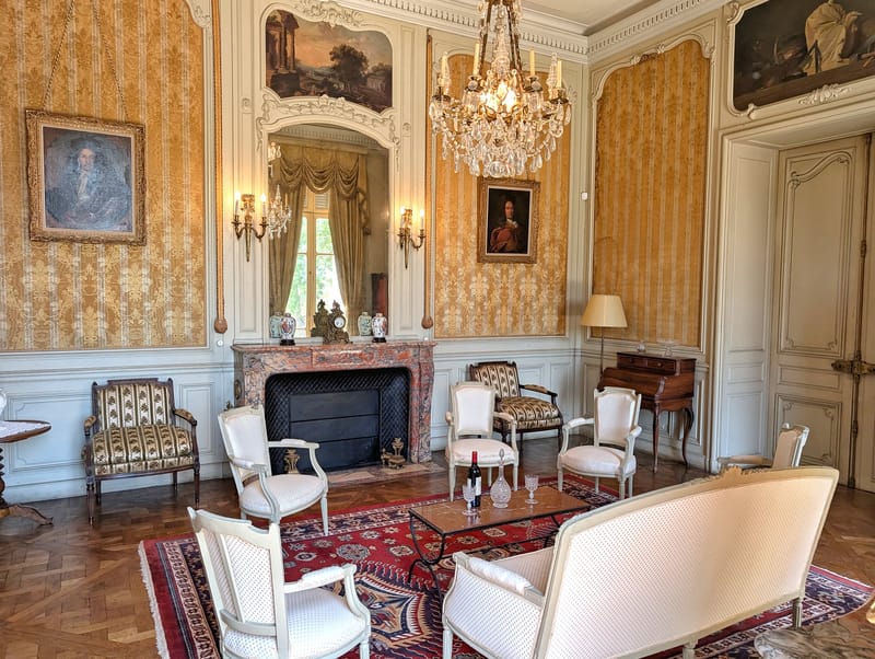 Château du Terral salon with framed paintings, fireplace, chandelier and upholstered armchairs