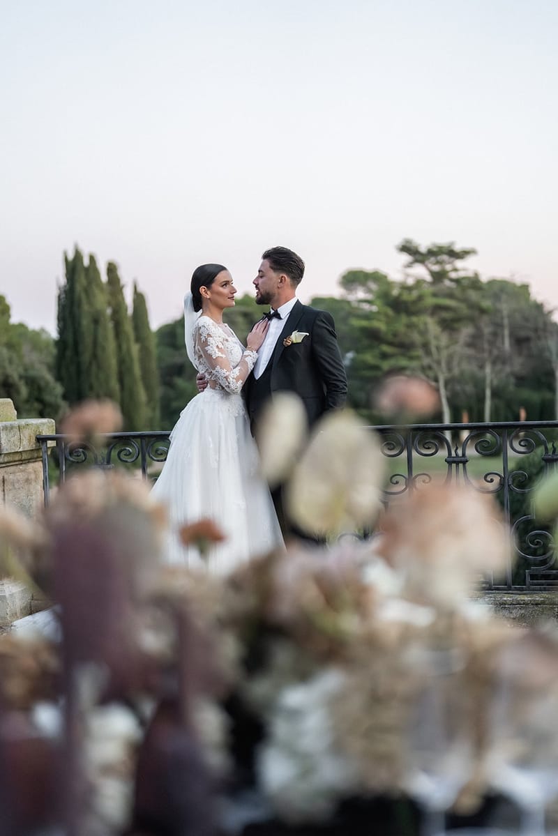 Bride and groom on a Château du Terral terrace at dusk behind a dried-flower arrangement