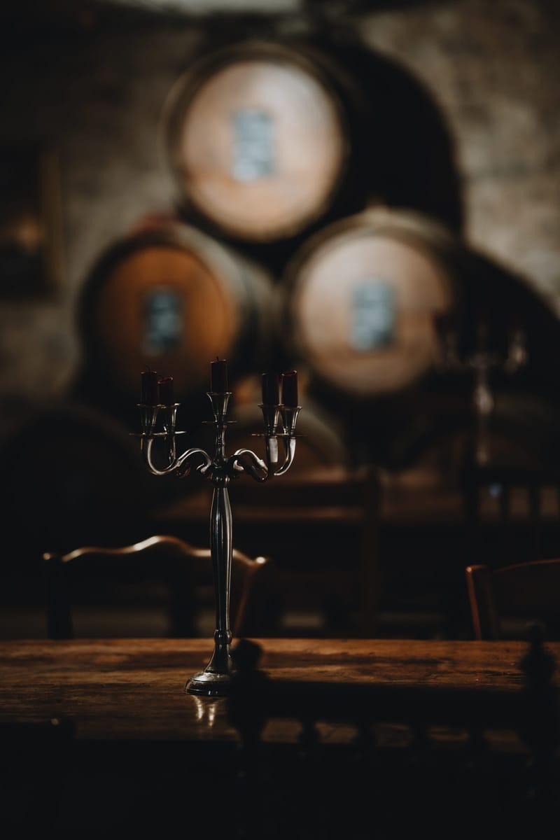 Silver candelabra with lit candles on a wooden table in front of wine barrels