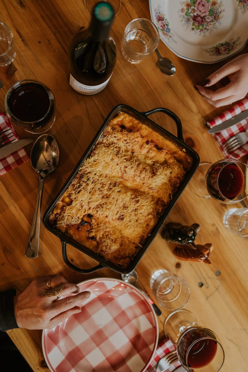 Overhead shot of a baked gratin dish on a wooden table with wine glasses and a Fleurie wine bottle