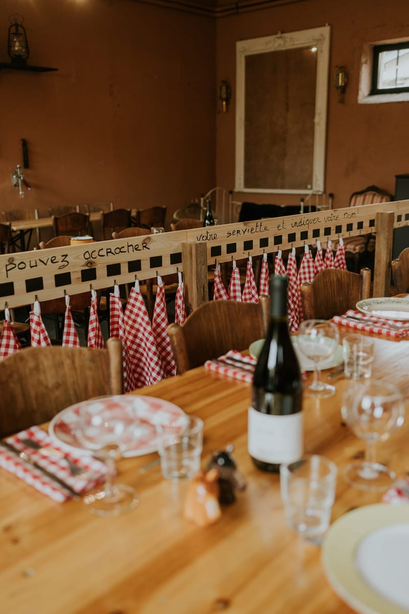 Table set with gingham napkins and a wine bottle in La Cantine du Vendangeur, guest napkins hanging on a rail behind
