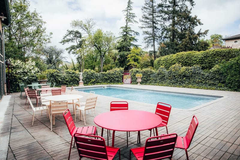 Poolside terrace with colourful bistro tables and chairs, ivy hedge and statue behind