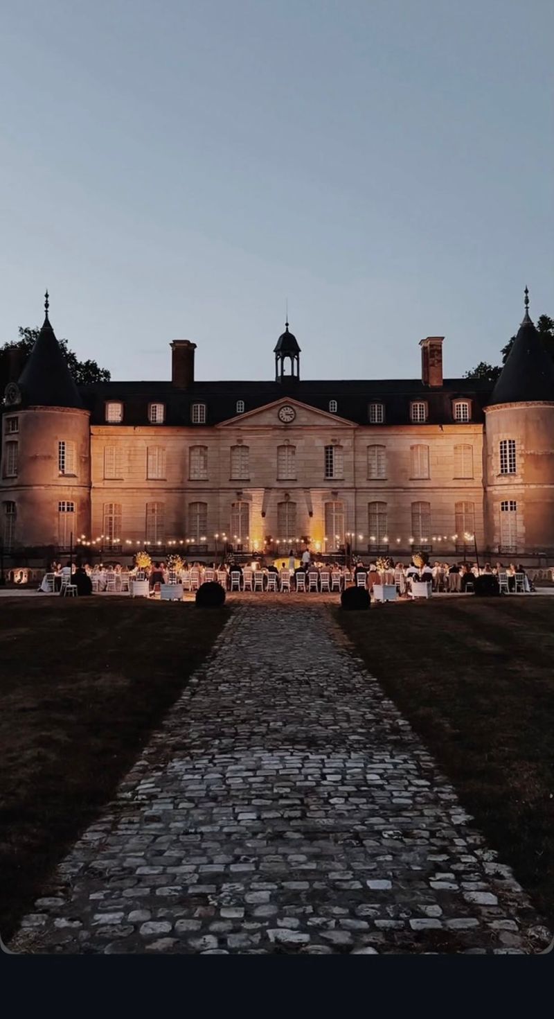 Evening wedding reception dinner in front of the château at Domaine de Verderonne, guests seated under string lighting.