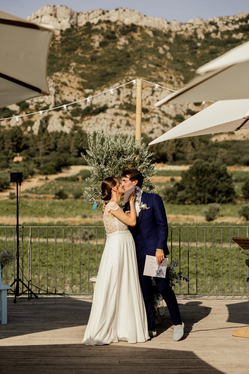 A couple kiss during their ceremony on the terrace at Domaine ODDO Vallon des Glauges, with vineyards and the Alpilles behind