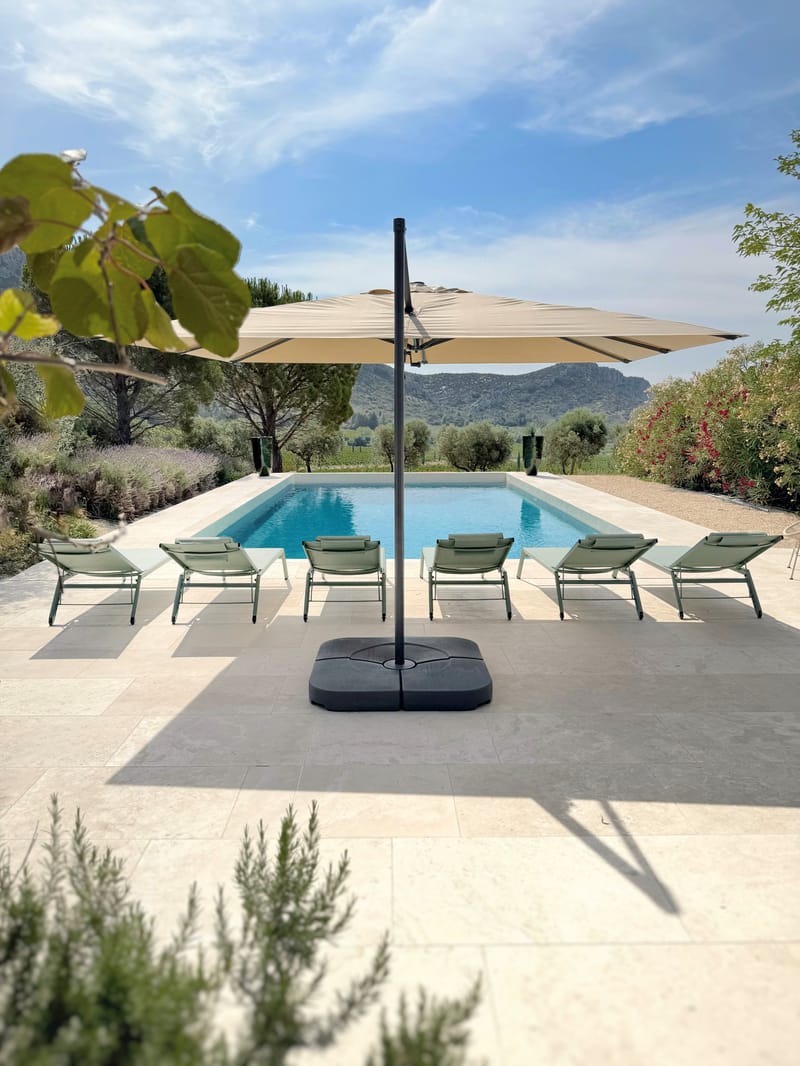 The swimming pool at the Villa des Glauges with sun loungers and a large parasol, framed by Mediterranean planting