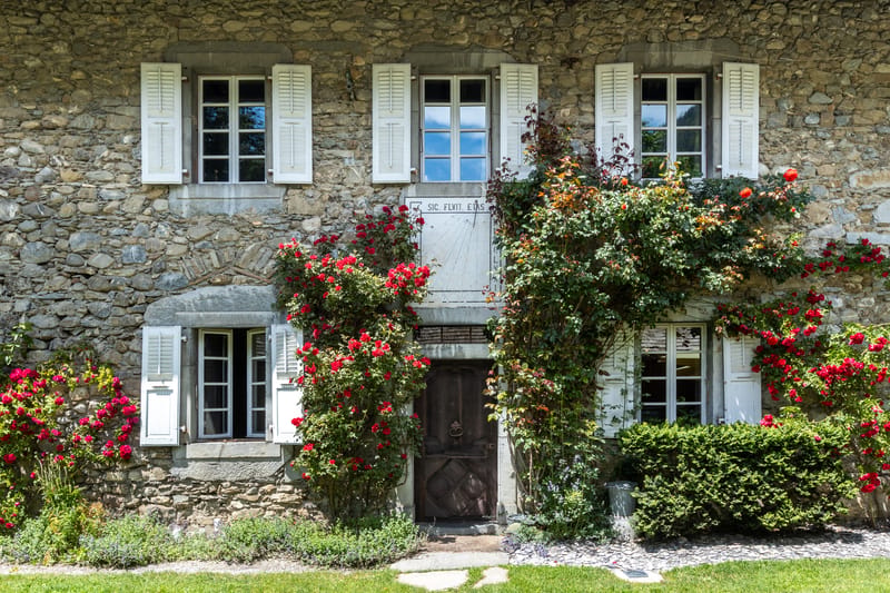 Stone facade of Hotel Coutettaz with white shutters and climbing roses