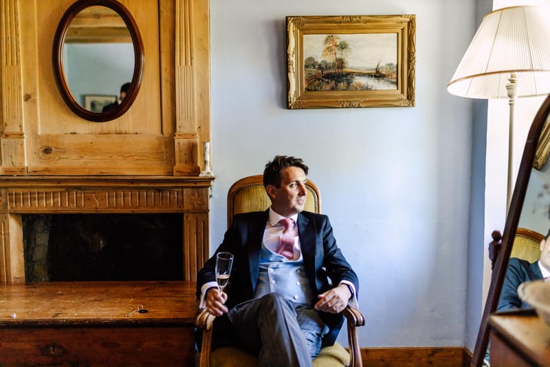 Groom seated by a carved wooden fireplace and mirror in a salon