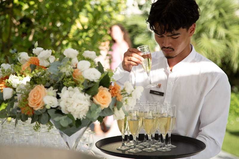 Waiter pouring Champagne beside a bouquet of white and peach roses in the garden