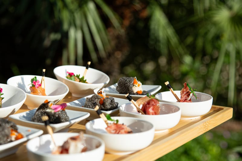 Canapés in small white bowls on a wooden tray in the garden