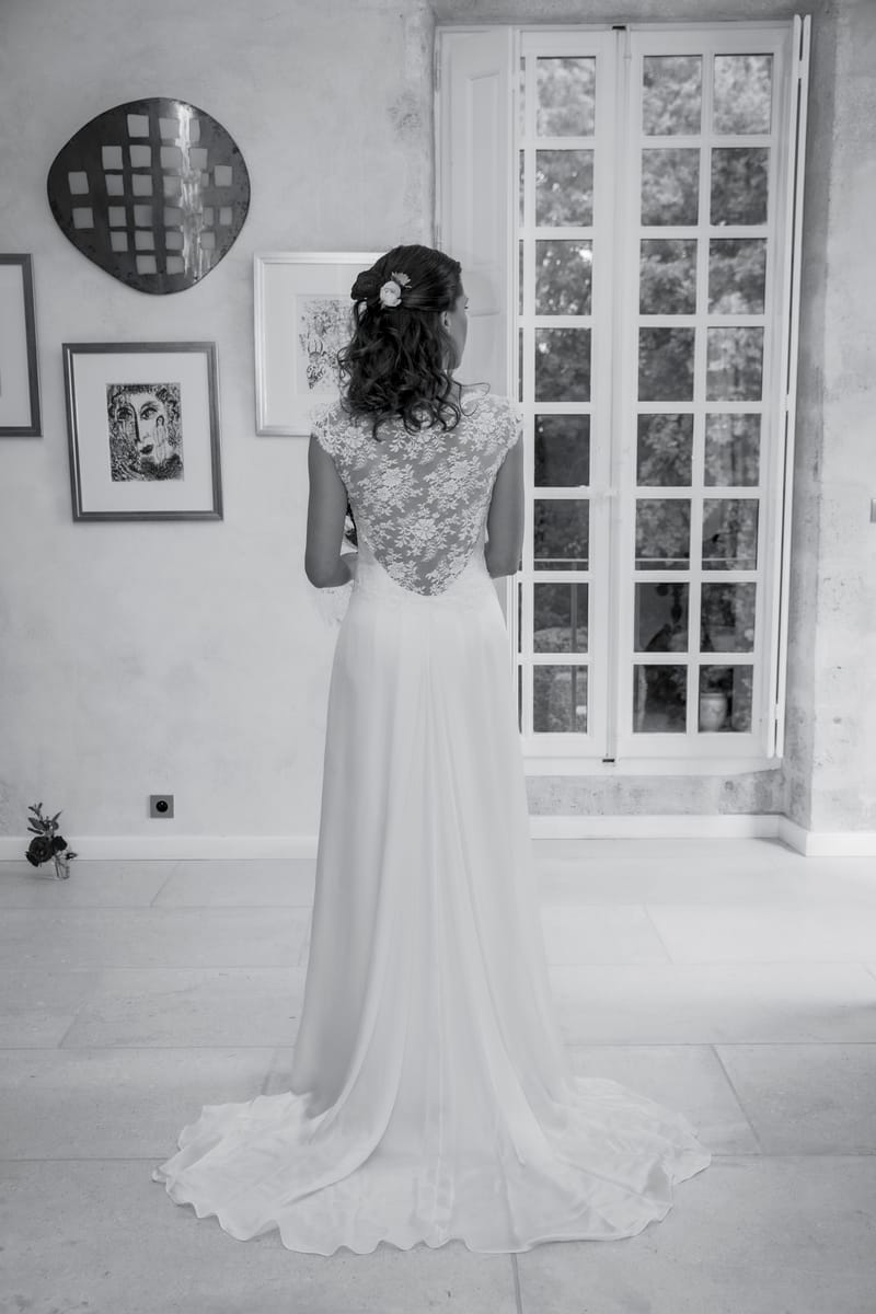 A bride at a tall French window in an interior room with artwork on the walls