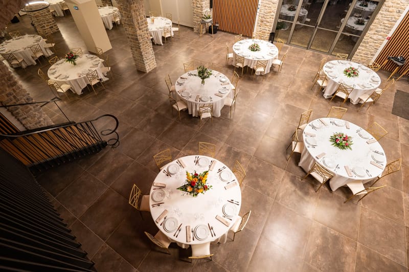 Overhead view of indoor reception hall with round tables and gold chairs at Domaine de Blacailloux