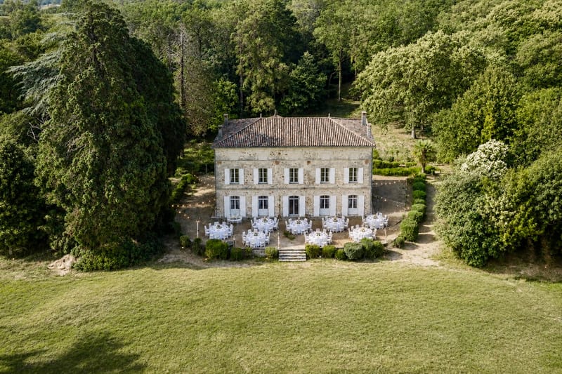 Aerial view of round dinner tables and string lights on the gravel forecourt in front of the château