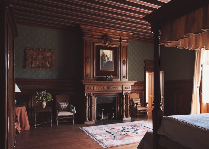 Wood-panelled bedroom with a carved fireplace, a portrait above it and green damask walls