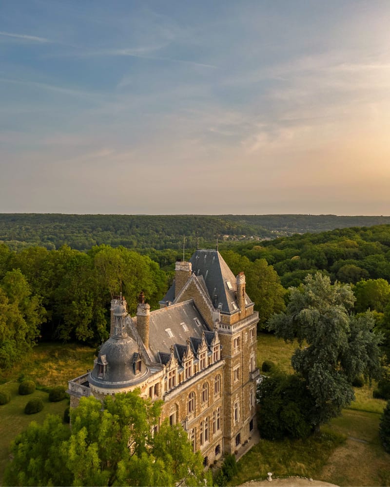 Aerial view of Château de Méridon at golden hour, surrounded by forest with sunset sky