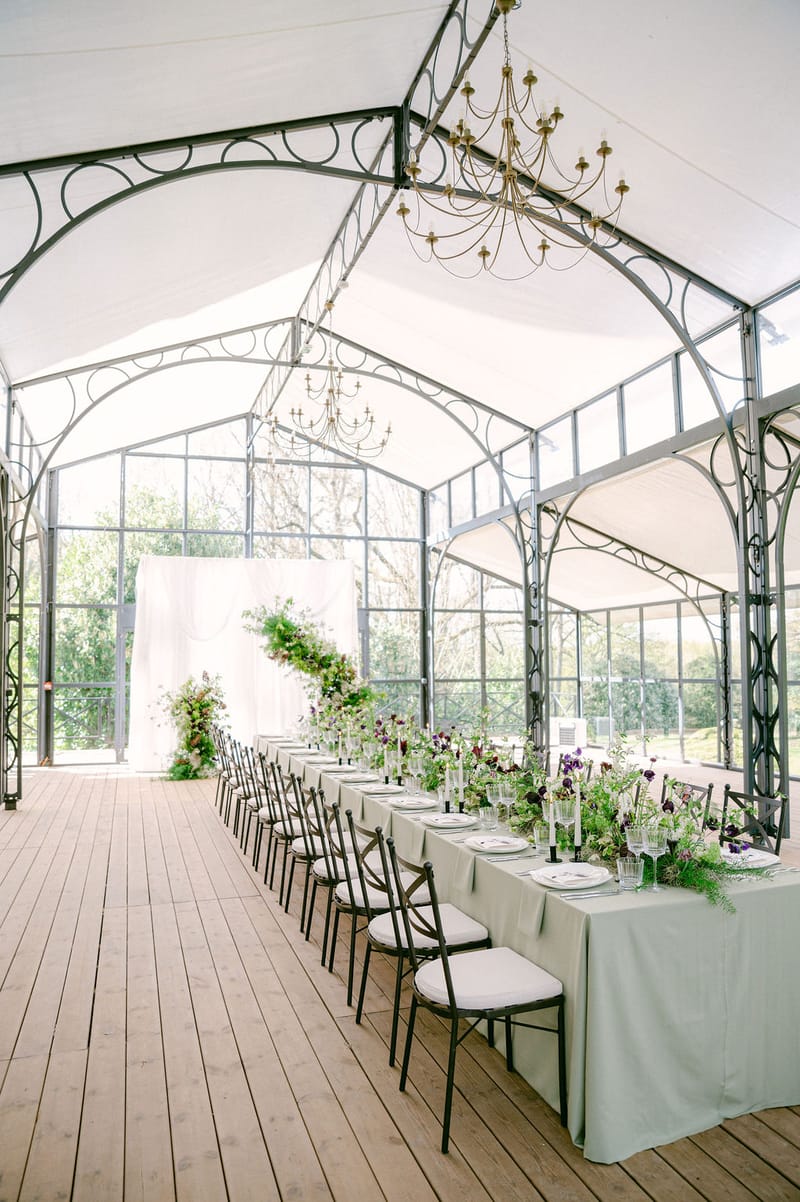 Crystal Glasshouse interior with gothic-arched wrought iron, golden chandelier, and long banquet table at Château de Méridon