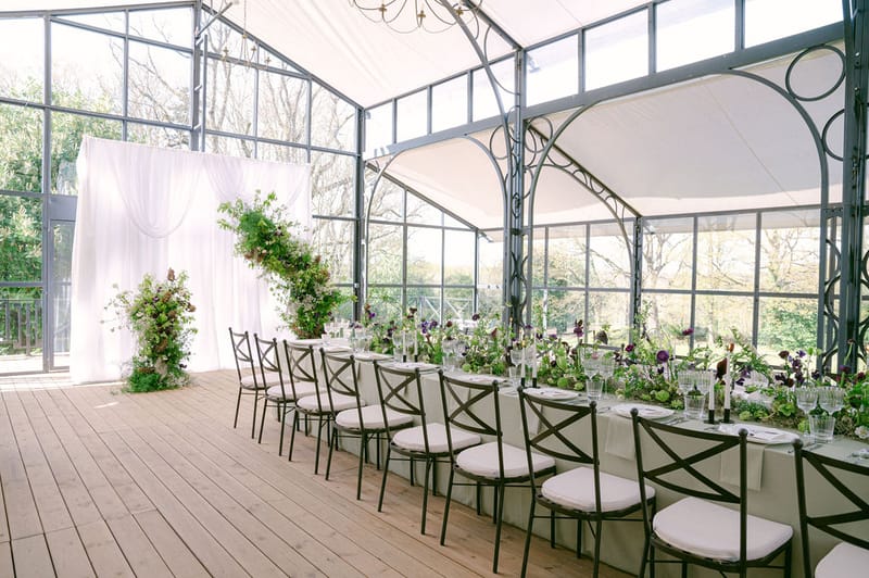Crystal Glasshouse interior at Château de Méridon — long banquet table with floral arch and full glass walls