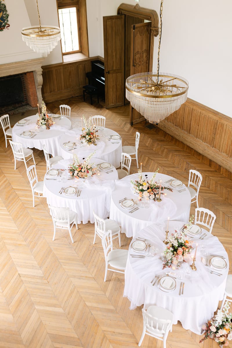 Château salon with parquet flooring, chandeliers, and round white tables set for wedding reception at Château de Méridon