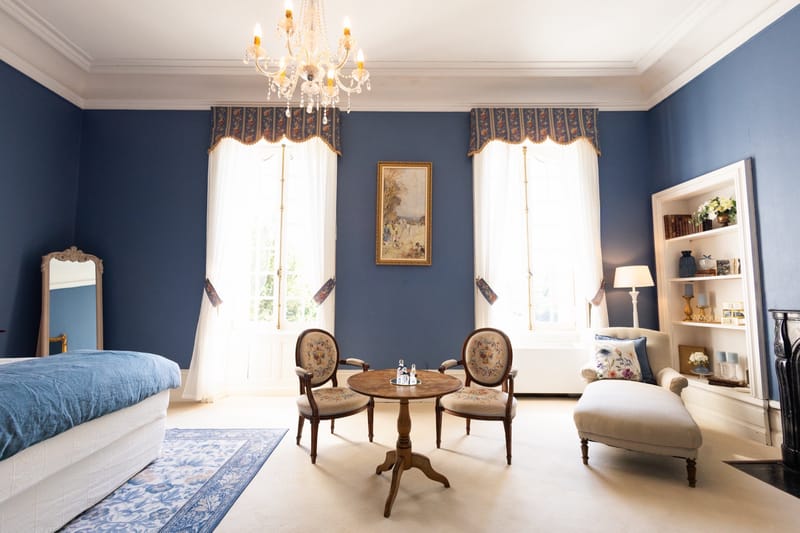 Blue-walled bridal suite at Chateau du Pordor with a crystal chandelier, a pair of armchairs by the window and a chaise longue
