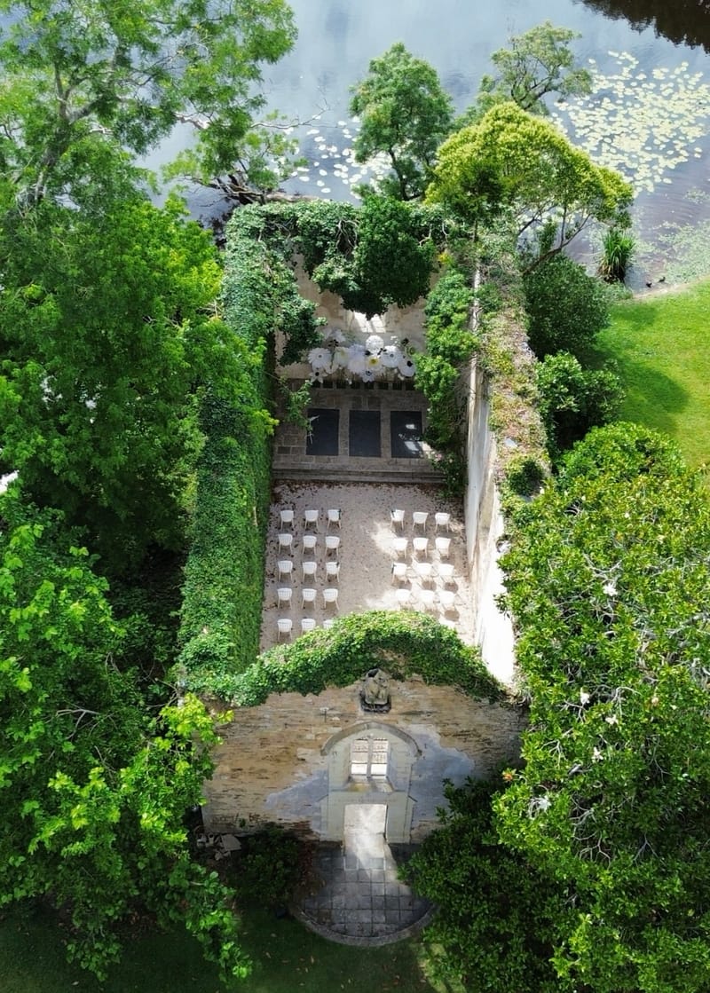 The roofless stone chapel at Chateau du Pordor seen from above, open to the sky with the lake beyond