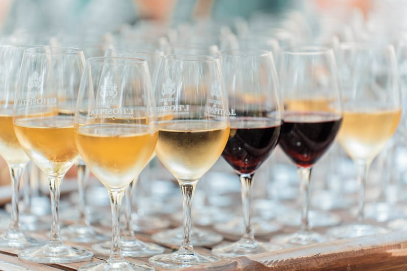 Row of branded Chateau L'Hospital wine glasses filled with white and red wine from the estate vineyard