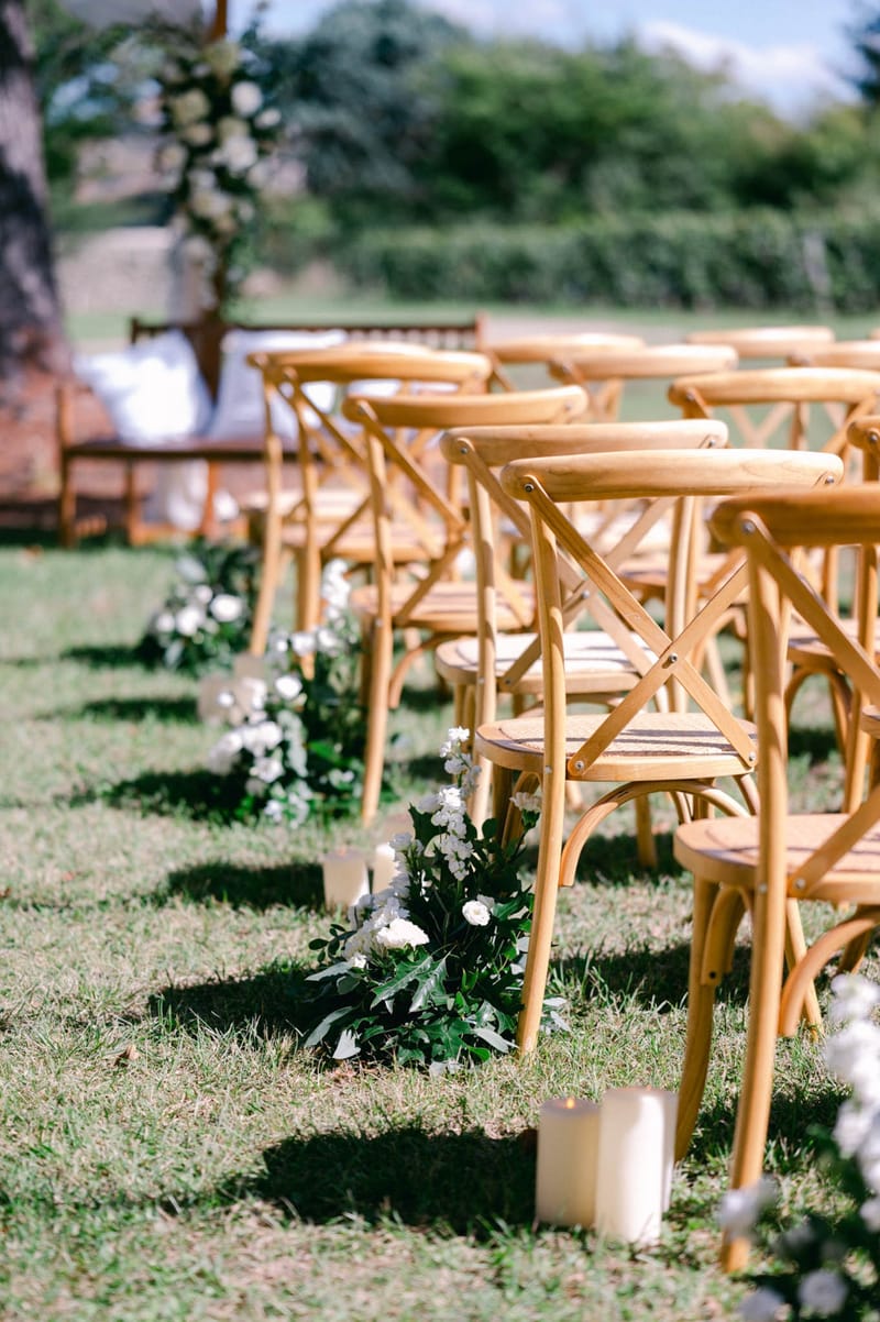 Ceremony aisle with cross-back chairs, pillar candles and floral pedestals set in the walled park