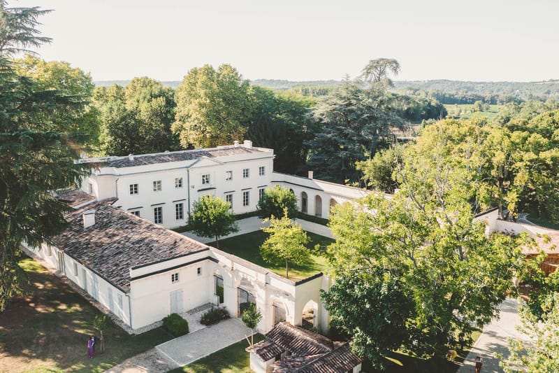 Aerial view of Chateau de l'Hospital estate with outbuildings and distant woodland