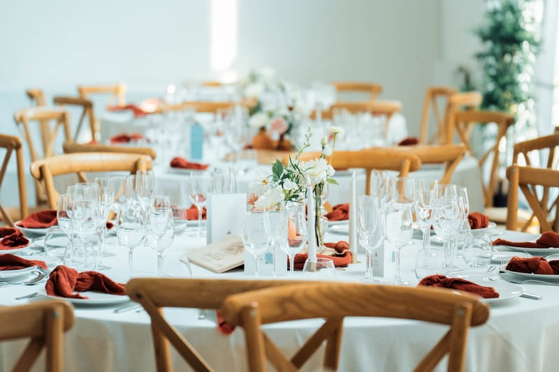 Close-up of a round dining table in the Orangery Hall with terracotta napkins, ivory florals, candles and menu cards