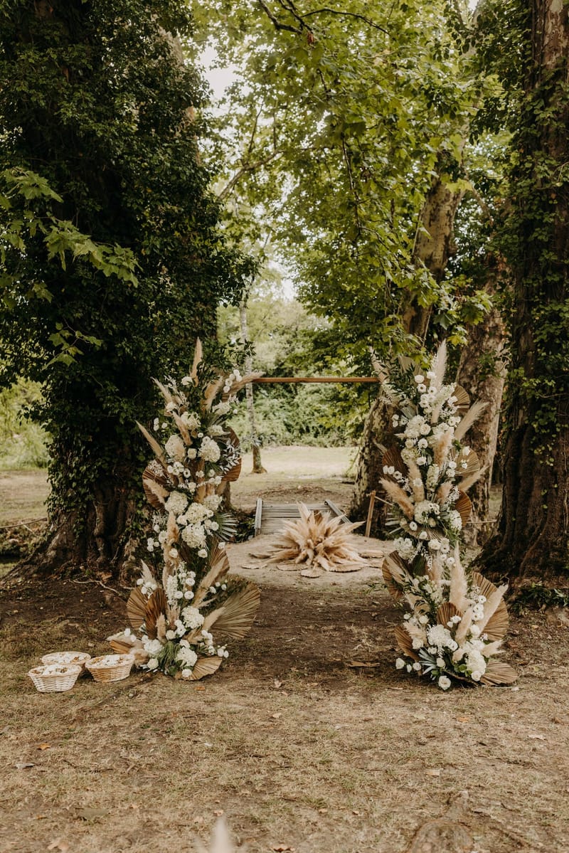 Boho ceremony arch of pampas grass and bloomed florals beneath the trees at Chateau de l'Hospital