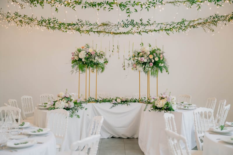 Orangery Hall at Chateau de l'Hospital set with a fairy-light greenery canopy, tall floral centrepieces and long wooden tables