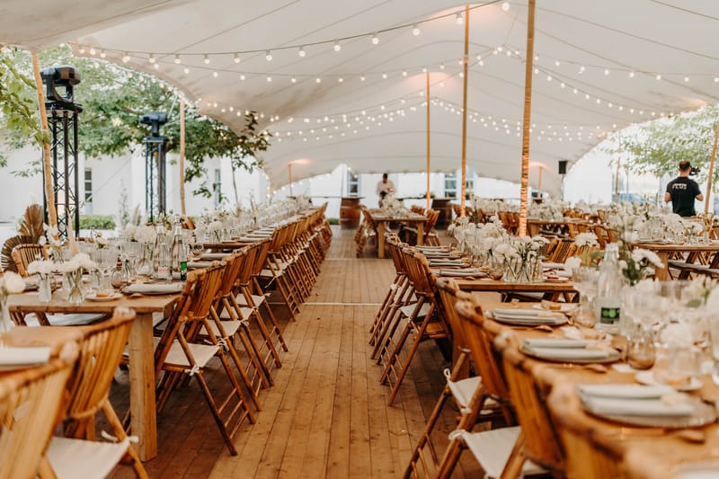 Stretch tent reception at Chateau de l'Hospital with long wooden tables, candles and festoon lighting