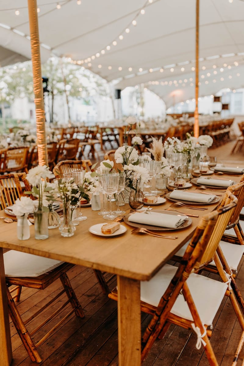Stretch tent dining at Chateau de l'Hospital with wooden tables, floral runners and amber glassware
