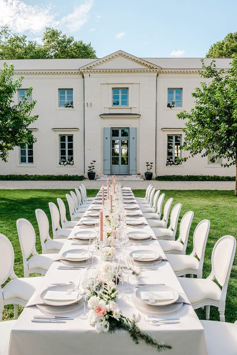 Long outdoor dinner table set on the lawn in front of the main facade of Chateau de l'Hospital