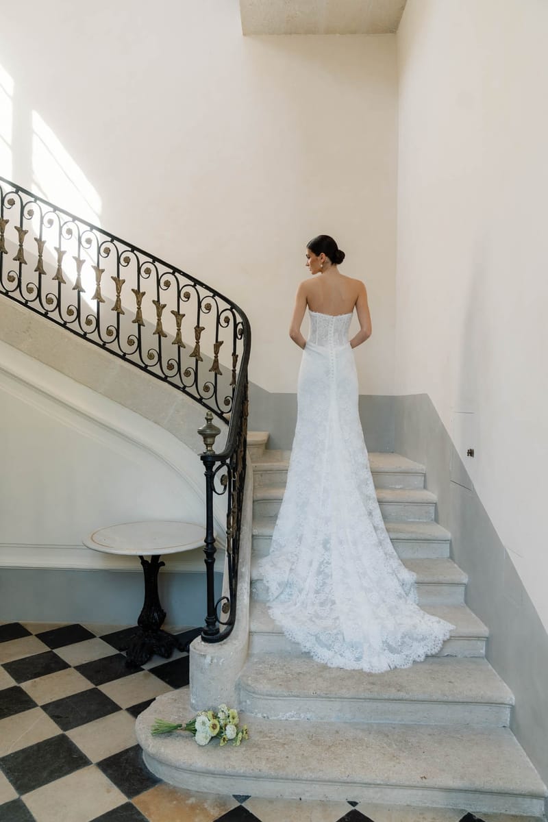 Bride standing on the chequerboard marble stair landing at Chateau de l'Hospital with the wrought-iron balustrade