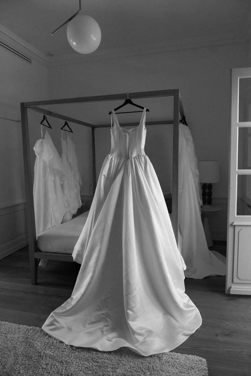 Black-and-white image of a wedding gown hanging on a four-poster bed in a Château de l'Hospital suite