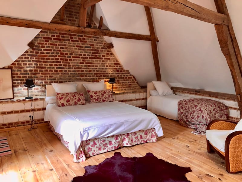 An attic guest room with a double and a single bed under exposed beams and brick
