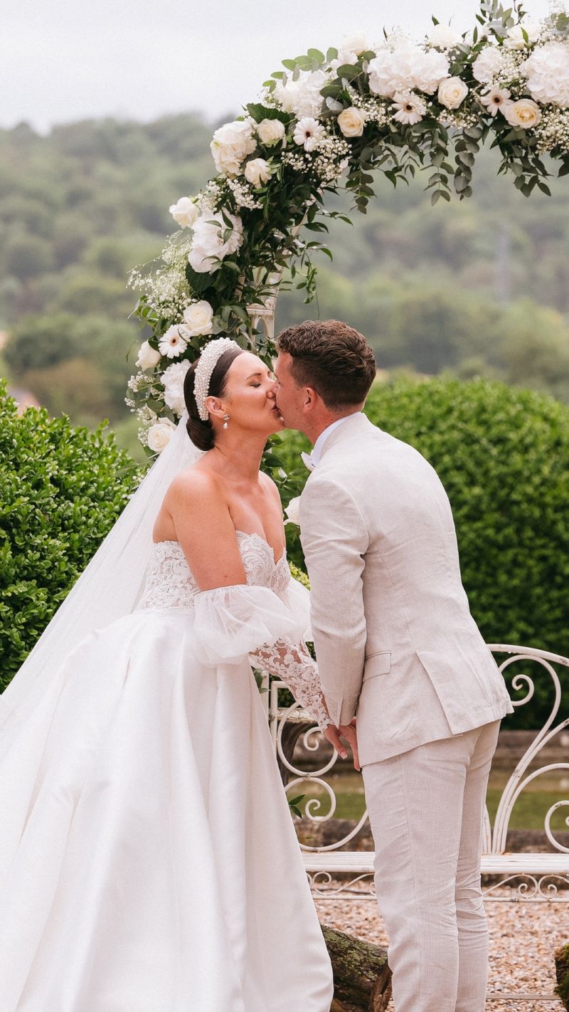A white and green floral ceremony arch set against the garden hedging