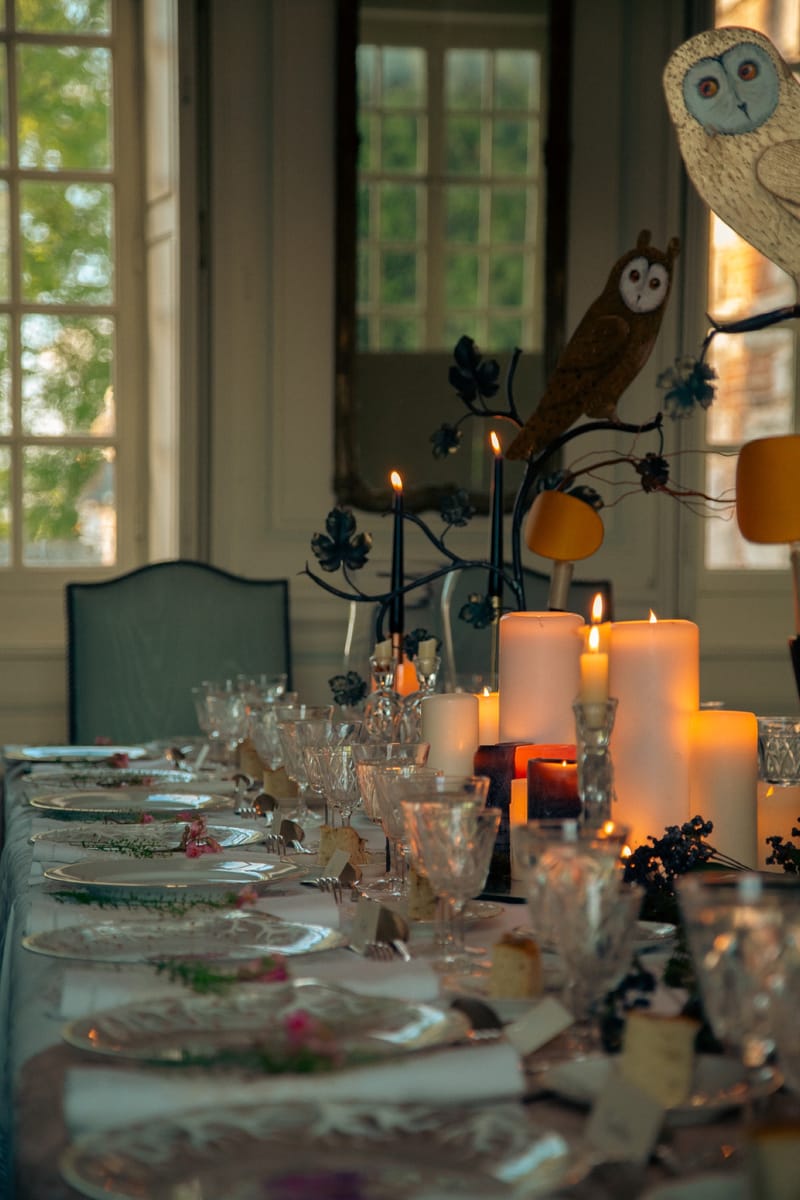 A long dining table lit with pillar candles in a room with tall windows